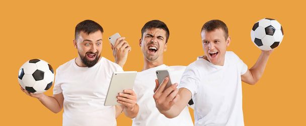 Collage of happy men with soccer balls, mobile phones and tablet computer on orange background - 写真・画像