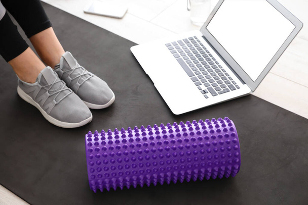 Woman with foam roller and laptop on mat at home, closeup - Photo, image