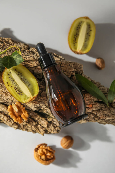 Композиція з пляшкою ефірної олії, ківі, волоських горіхів та кори дерева на світлому фоні
 - Фото, зображення