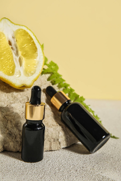 Bottles of essential oil, lemon and stone on table, closeup - 写真・画像