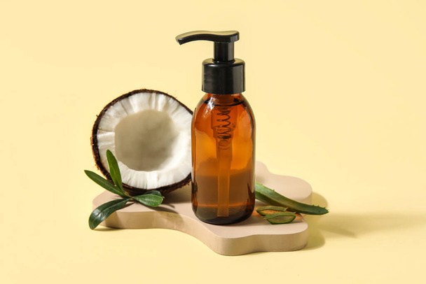Bottle of natural cosmetic product and coconut on color background - 写真・画像