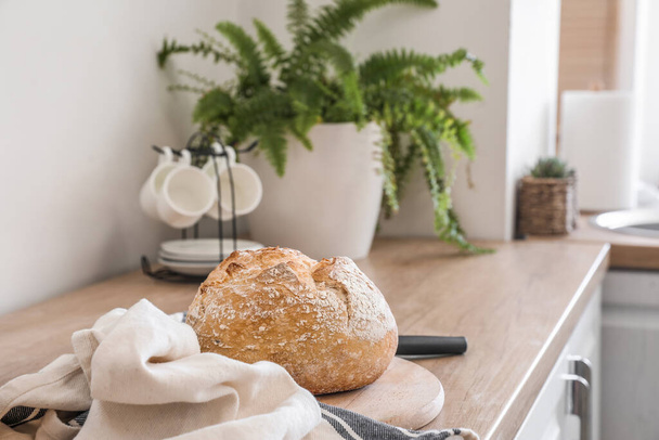 Доска для резки со свежим хлебом и салфеткой на кухонном столе возле светлой стены - Фото, изображение