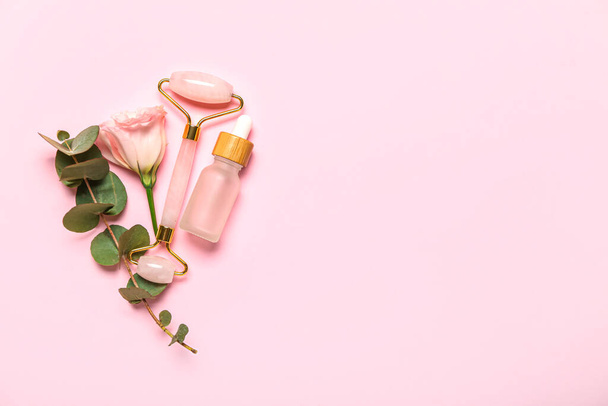 Facial massage tool with cosmetic bottle, eucalyptus and rose on pink background - Foto, Imagen