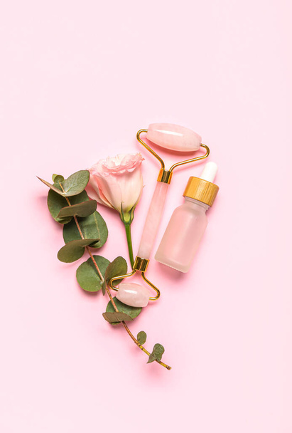 Facial massage tool with cosmetic dropper bottle, eucalyptus and rose on pink background - Foto, afbeelding