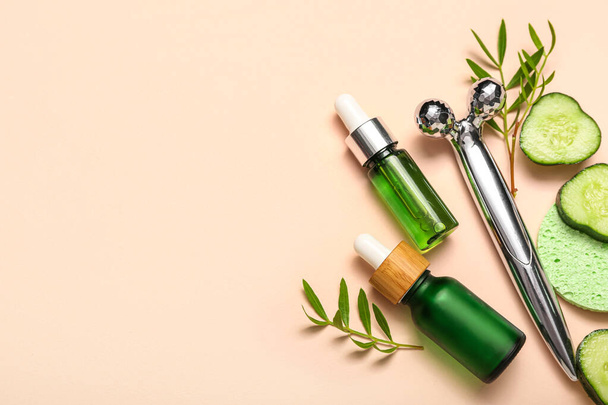 Facial massage tool with cosmetic dropper bottles, cucumber slices and plant branches on beige background - Foto, imagen