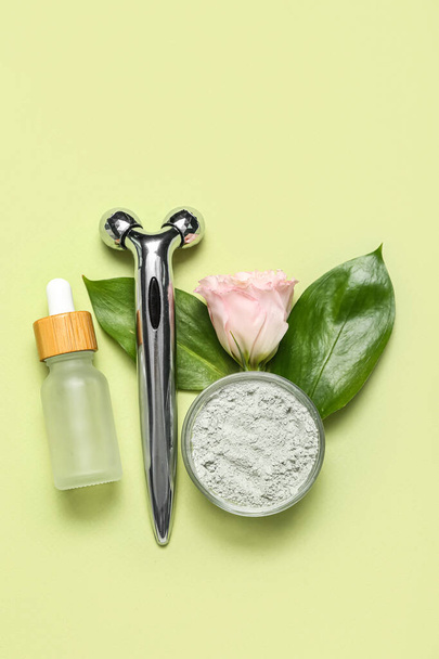 Facial massage tool with cosmetic dropper bottle, clay, rose and leaves on green background - Foto, imagen