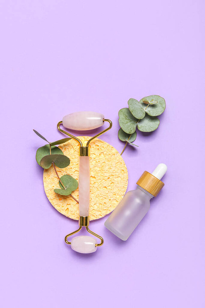 Facial massage tool with cosmetic dropper bottle, sponge and eucalyptus branches on lilac background - Foto, Imagen