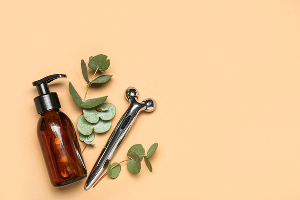 Facial massage tool with cosmetic bottle and eucalyptus branches on beige background - Foto, Imagen