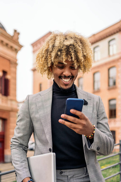 Happy black business man with afro hair and cool suit using his mobile phone in the city. - Fotoğraf, Görsel