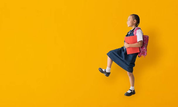 Asian student child girl wears school uniform holding book with walking, isolated on yellow background with Clipping paths for design work empty free space - Foto, Imagen