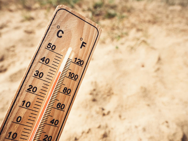 Wooden thermometer showing high temperatures over 36 degrees Celsius on sunny day on background of dry sandy ground. Concept of heat wave, warm weather, global warming, climate. - Fotografie, Obrázek