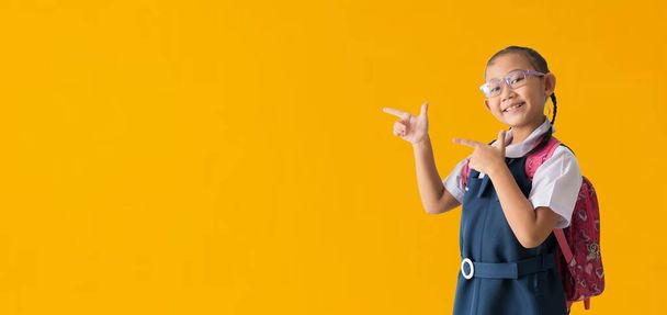 Asian student girl wears school uniform pointing fingers at copy space over yellow background. isolated Clipping paths for design work empty  - Foto, Imagem