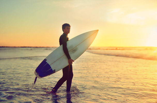 I surf, therefore I am. a young surfer walking into the water with his surfboard under his arm - 写真・画像