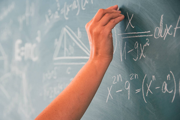 Close-up shot of a hand holding chalk and writing mathematical equations on the blackboard. Education concept. - Foto, Bild