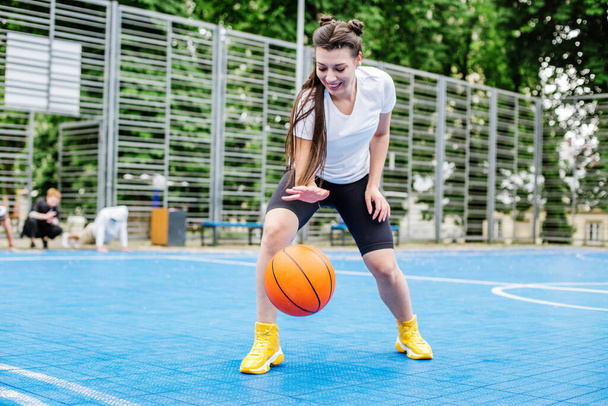 Концепция спорта, хобби и здорового образа жизни. Молодая спортсменка тренируется играть в баскетбол на современной открытой баскетбольной площадке. - Фото, изображение