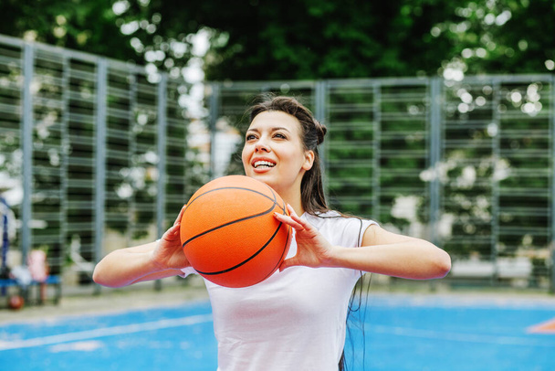 Concept van sport, hobby 's en gezonde levensstijl. Jonge atletische vrouw is de opleiding om basketbal te spelen op moderne outdoor basketbalveld. - Foto, afbeelding