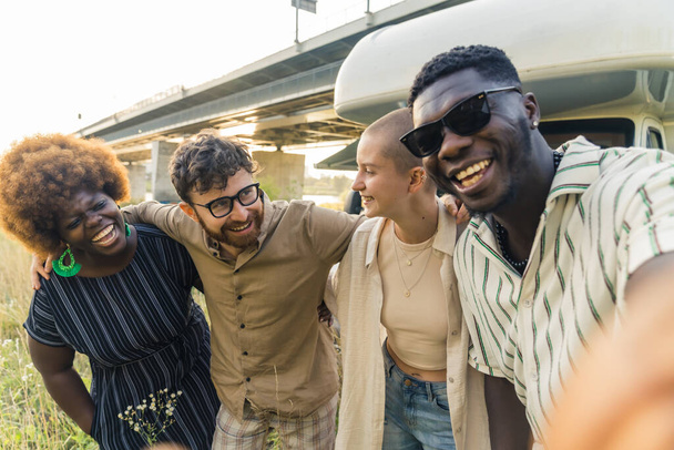Interracial friendship. Group of happy close friends, reunited on their camping van trip, traveling through the country. Laughing and taking selfies together near the river. High quality photo - Photo, Image