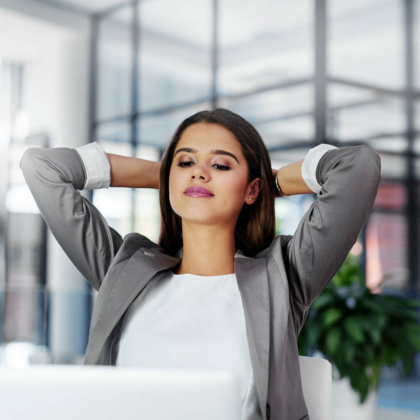 No better feeling than seeing the end of your deadlines. a young businesswoman sitting with her hands behind her head at her office desk - Valokuva, kuva