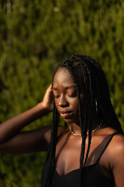 Portrait of a young black female removing her hair from her face whit her eyes closed during a sunset modeling session - Valokuva, kuva