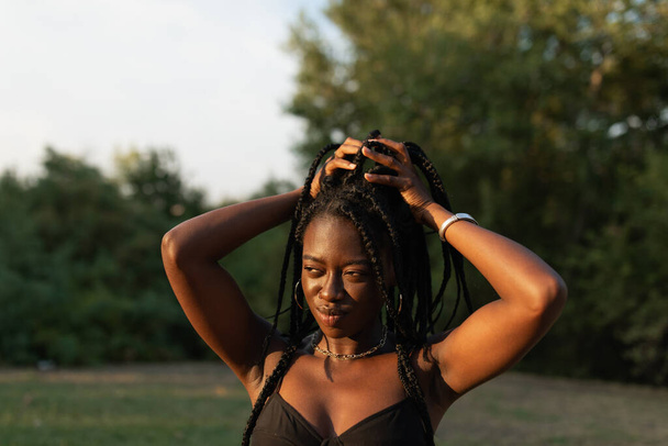 Portrait of a young black female holding her braids in a ponytail at the park during a summer sunset - Fotó, kép