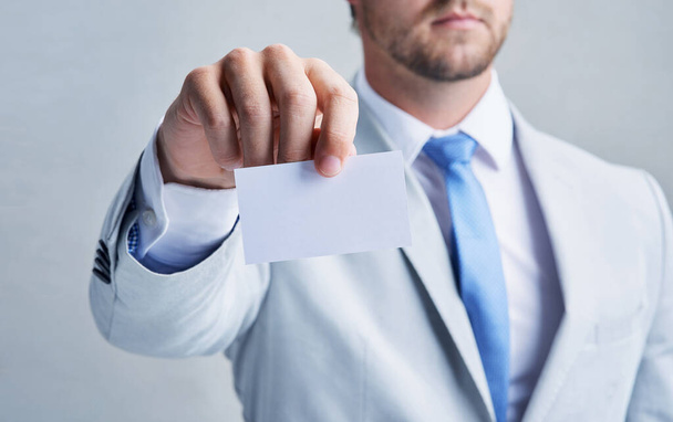Im giving you something you cant find anywhere else. Studio shot of a businessman holding up a blank business card against a grey background - Foto, immagini