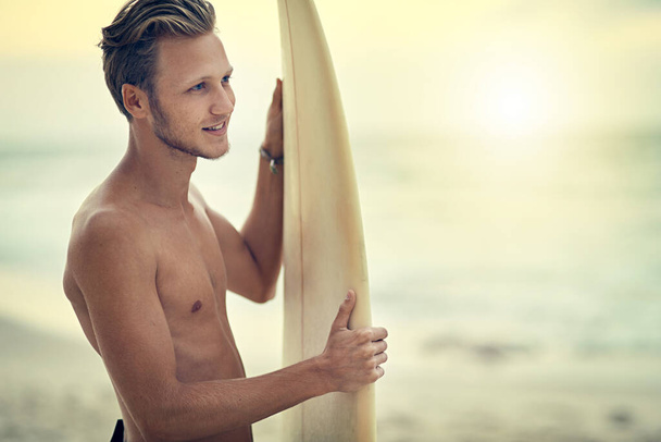 Взятие в движение океана. молодой серфер без рубашки наблюдает за волнами, держа свою доску для серфинга на пляже - Фото, изображение