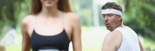 Толстяк смотрит на молодую спортсменку, бегающую в парке. Концепция здорового образа жизни - Фото, изображение