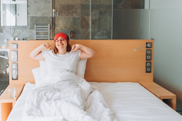 Kaunis onnellinen punapää nainen herää sängyssään, hymyilee ja venyttelee. Millennial valkoihoinen tyttö venyttää herätä kodikas valkoinen sänky kotona - Valokuva, kuva