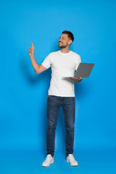 Happy man with laptop on light blue background - Photo, Image
