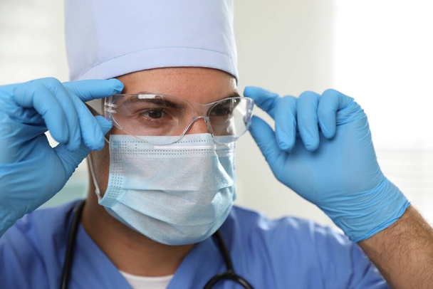 Doctor in protective mask, glasses and medical gloves against light background - 写真・画像