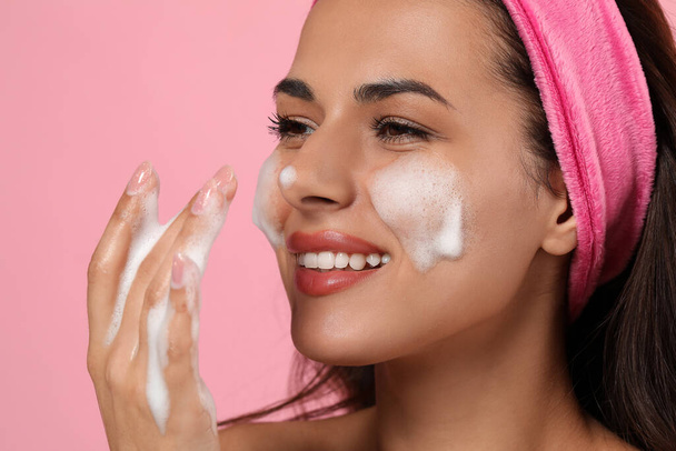 Beautiful woman applying facial cleansing foam on pink background, closeup - Fotó, kép