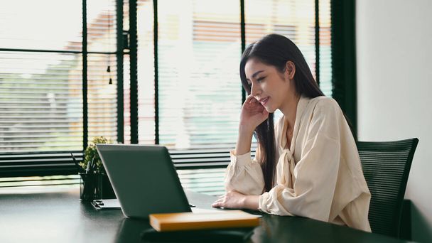 Πανέμορφη γυναίκα επιχειρηματίας κάθεται στο σύγχρονο γραφείο της και τον έλεγχο των πληροφοριών σχετικά με το φορητό υπολογιστή. - Φωτογραφία, εικόνα