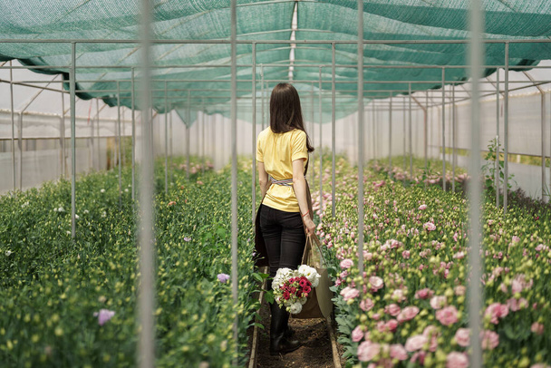Γυναίκα ανθοπώλης περπάτημα μεταξύ των λουλουδιών σε ένα πράσινο σπίτι μεταφέρουν ένα καλάθι με ένα φρέσκο μπουκέτο - Φωτογραφία, εικόνα