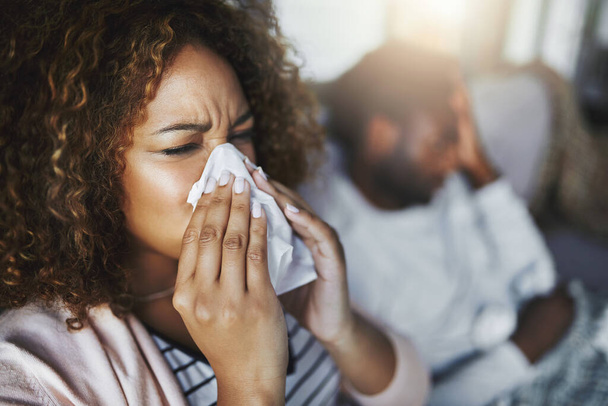 Its the height of cold and flu season. a young woman blowing her nose with her boyfriend in the background - Foto, imagen