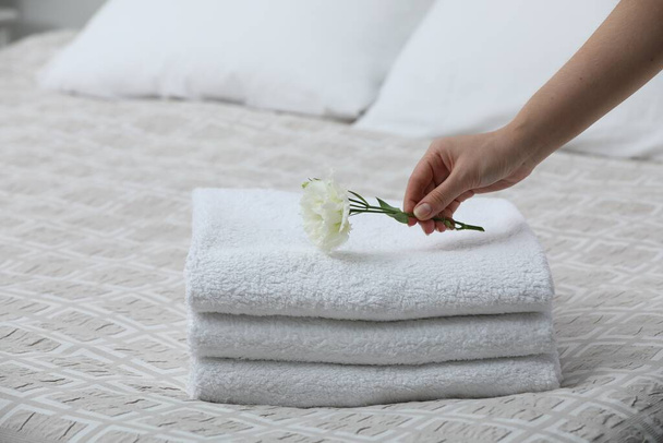 Woman putting Eustoma flower on folded towels in bedroom, closeup - Фото, изображение