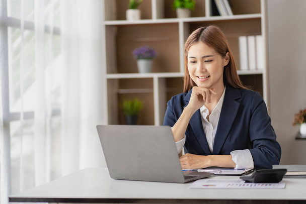 Charming Asian businesswoman or finance worker using a laptop computer and working on financial accounting reports in the office. - 写真・画像