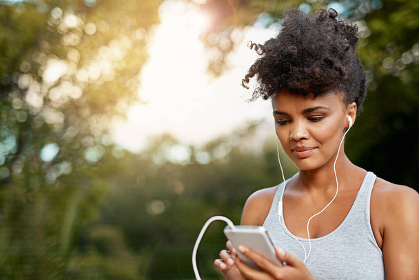 This playlist will get me moving. a young woman listening to music on her phone while out for a run - Foto, afbeelding