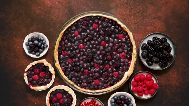 Homemade fresh round cake tart with berries, raspberries, blackberries, red and black currant jelly. Top view, flat lay on dark rustit table - Filmati, video