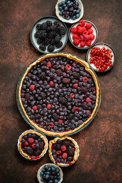 Homemade fresh round cake tart with berries, raspberries, blackberries, red and black currant jelly. Top view, flat lay on dark rustit table - Fotoğraf, Görsel