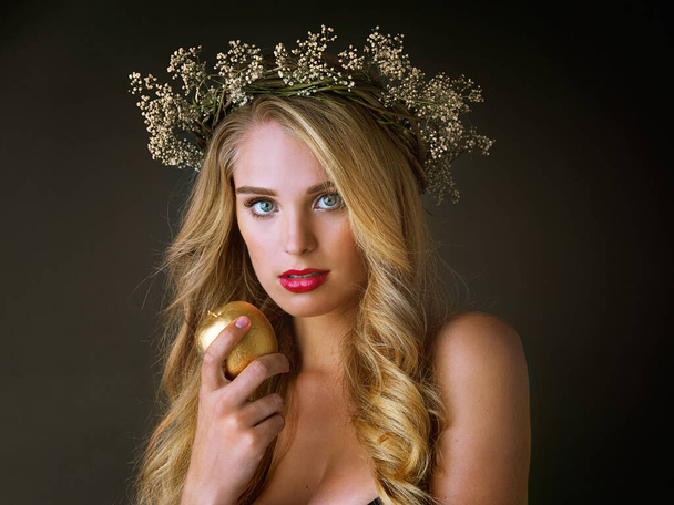 Κάθε θεά αξίζει χρυσό. Στούντιο πλάνο μιας πανέμορφης νεαρής γυναίκας που τρώει ένα χρυσό μήλο σε σκούρο φόντο - Φωτογραφία, εικόνα