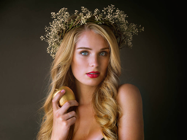 Фрукты подходят для самых красивых из них. Студийный снимок великолепной молодой женщины, поедающей золотое яблоко на тёмном фоне - Фото, изображение