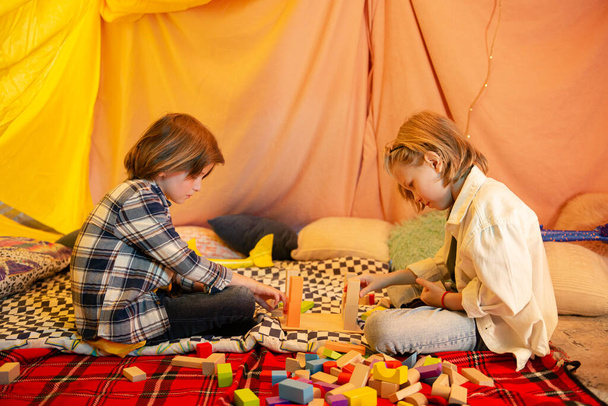 Two youthful boys are playing joyfully together with airplanes and making them crash into each other all while being in a big blanket tent. - 写真・画像