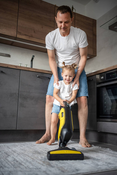 Father and daughter having fun with vacuum cleaner while cleaning at home kitchen. High quality photo - Foto, immagini