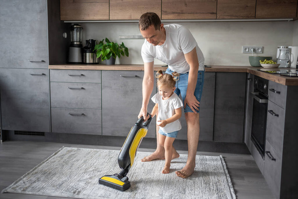 Father and daughter having fun with vacuum cleaner while cleaning at home kitchen. High quality photo - 写真・画像