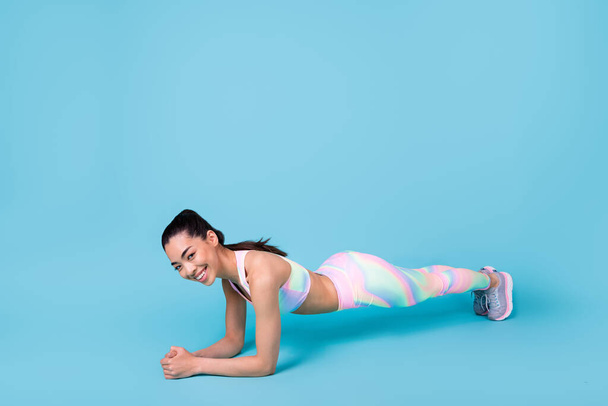 Full size photo of strong cute japanese lady trainer stand plank smiling wear trendy sportive look isolated on bright blue color background. - 写真・画像