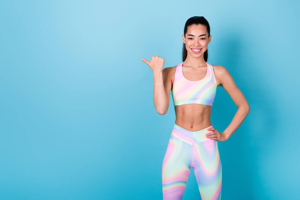 Photo portrait of pretty chinese woman direct empty space smiling dressed stylish sporty clothes isolated on bright blue color background. - 写真・画像