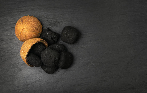Coconut coal briquette on black background. Pressed charcoal for braai, coconut barbecue coal, bbq briquettes, grill charcoal top view - Foto, imagen