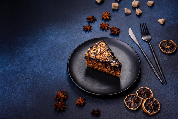 A piece of fresh delicious cake with nuts and chocolate on a black plate against a dark blue background. Desserts and sweets to the dinner table - Zdjęcie, obraz
