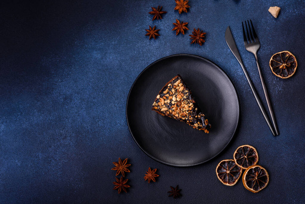 Кусок свежего вкусного торта с орехами и шоколадом на черной тарелке на темно-синем фоне. Десерты и сладости к обеденному столу - Фото, изображение