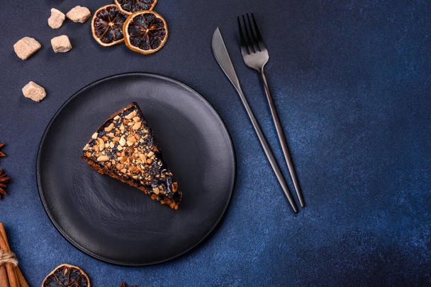 A piece of fresh delicious cake with nuts and chocolate on a black plate against a dark blue background. Desserts and sweets to the dinner table - Photo, Image